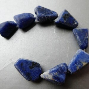 May include: A strand of eight irregular, tumbled lapis lazuli beads in a deep royal blue color with subtle black and white mineral inclusions. The stones are strung on a thin, clear filament, arranged in a circular formation for display.