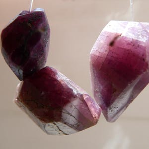 Könnte beinhalten: Drei facettierte rosafarbene und violette Edelsteinperlen mit glänzender, durchscheinender Oberfläche.