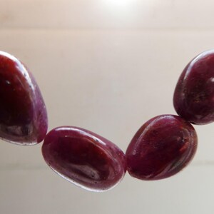 May include: A strand of five polished, oval-shaped, deep burgundy gemstones. The stones are strung together with a thin, clear string. The text "No 1" is in the lower left corner.