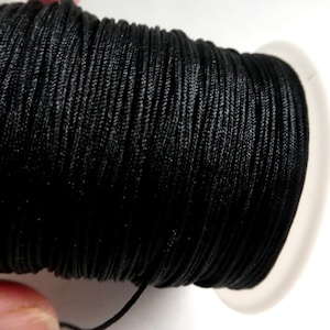 May include: A spool of black nylon cord. The cord is tightly wound on a white plastic spool. The black cord has a slight sheen, and a single strand extends from the spool.