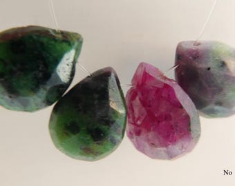 Op de afbeelding: Vier edelsteen kralen aan een touwtje. Twee zijn groen met donkere insluitsels, één is gefacetteerd magenta en de laatste is een mix van groen en paars. De kralen zijn druppelvormig.