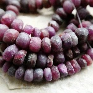 May include: A strand of purple gemstone beads. The beads are faceted and have a rough, irregular texture.