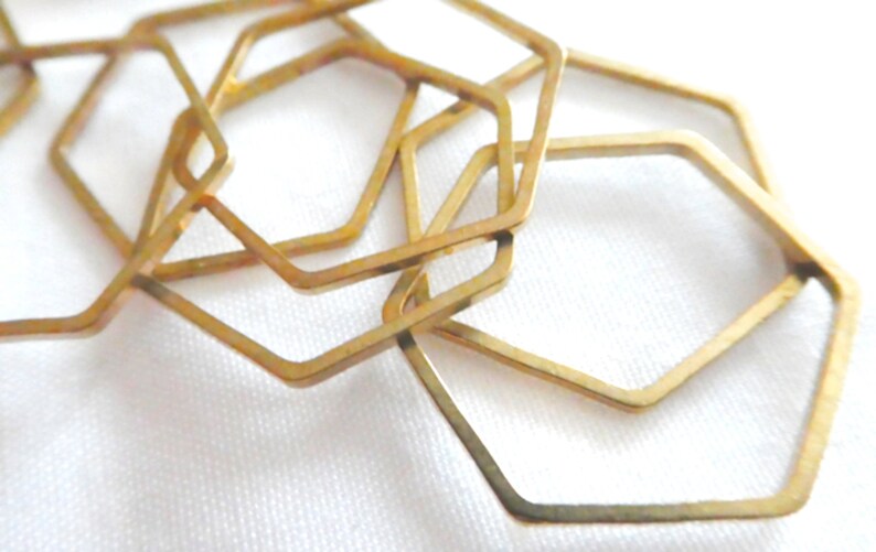 Peut inclure: Une collection de plusieurs hexagones en m&eacute;tal dor&eacute; &agrave; cadre ouvert dispos&eacute;s en un motif superpos&eacute;. Chaque pi&egrave;ce individuelle pr&eacute;sente une forme hexagonale g&eacute;om&eacute;trique fine et plate avec une surface lisse et r&eacute;fl&eacute;chissante.
