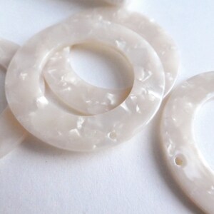 May include: White marbled plastic rings with a hole in the center. The rings are thick and have a smooth, glossy finish.