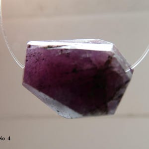 May include: A faceted, deep purple gemstone bead strung on a clear cord. The bead has a geometric shape with multiple facets, displaying a range of purple hues. The text "No 4" is visible in the lower left corner.