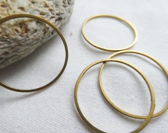 May include: Several gold-colored metal rings of varying sizes are arranged on a white surface, near a textured stone. The rings appear to be made of brass or a similar metal. The lighting is soft, highlighting the metallic sheen.