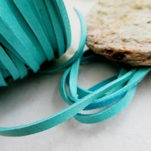 May include: Close-up of a roll of turquoise suede leather cord. The cord is unraveled in a loop, with a natural stone in the background. The cord is approximately 3mm wide, suitable for jewelry making and crafts.