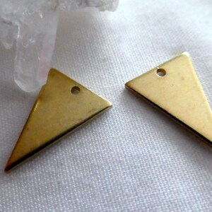 Op de afbeelding: Twee gouden driehoekige metalen bedels met een gat aan de bovenkant om te bevestigen aan sieraden of andere knutselwerkjes.