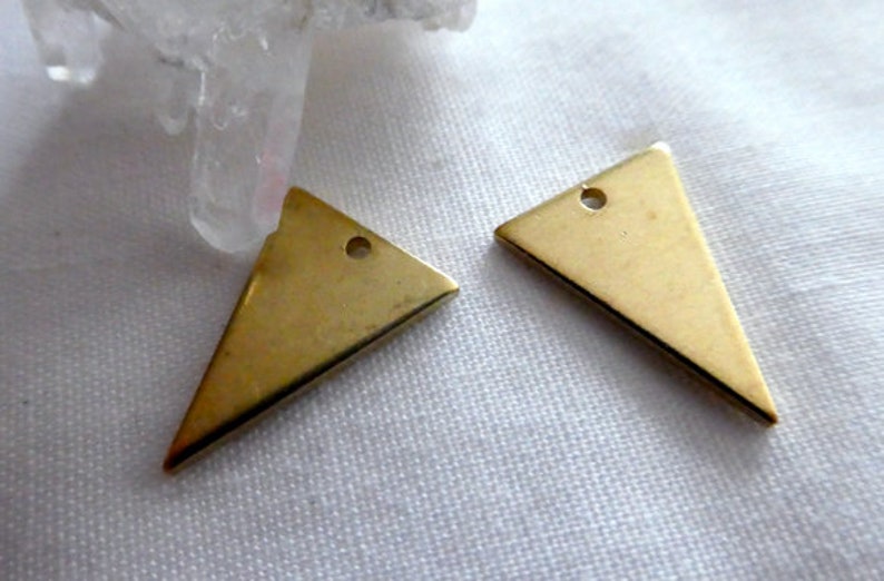 Op de afbeelding: Twee gouden driehoekige metalen bedels met een gat aan de bovenkant om te bevestigen aan sieraden of andere knutselwerkjes.