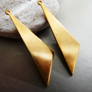 Puede incluir: Dos colgantes de pendientes de metal de color dorado, de forma triangular, con un bucle en la parte superior para sujetarlos a un cierre de pendiente.