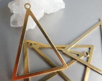 May include: Several gold-colored, open-frame triangle pendants with small holes at the top for stringing. The pendants are arranged in a slightly overlapping pattern. The background is a light gray surface with a white, crystalline object.