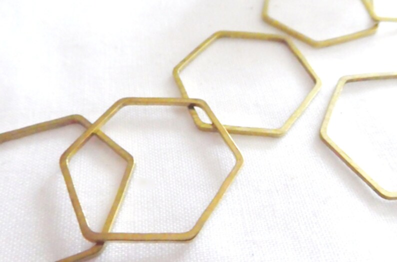 Peut inclure: Une collection de cadres hexagonaux en m&eacute;tal dor&eacute; fin dispos&eacute;s en un motif l&acirc;che et superpos&eacute;. Chaque cadre est une forme g&eacute;om&eacute;trique simple et ouverte avec une finition m&eacute;tallique lisse, cr&eacute;ant une s&eacute;rie de contours &agrave; six c&ocirc;t&eacute;s reli&eacute;s.