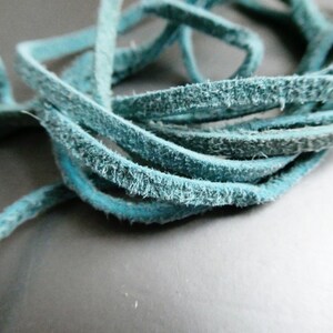 May include: Close-up of a bundle of turquoise suede leather cord. The cord is tightly coiled, revealing its soft, textured surface. The color is a vibrant teal, perfect for jewelry making or craft projects.