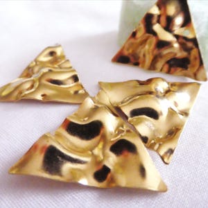 May include: Three triangular metal components with a polished gold finish and a hammered, rippled texture. Each piece features a reflective surface with irregular indentations, creating a wavy appearance across the flat, geometric shapes.