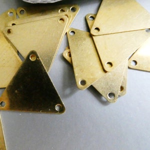 May include: A pile of gold-colored metal triangle shapes with holes in each corner. The triangles are stacked on top of each other.