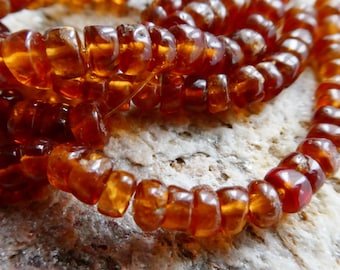 May include: Close-up of a strand of amber-colored beads. The beads are irregularly shaped and have a polished, translucent appearance. The beads are strung together, creating a necklace or bracelet.