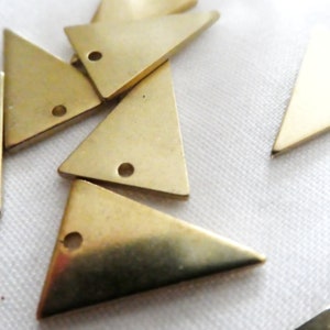 Op de afbeelding: Een groep van zeven goudkleurige metalen driehoeksvormen met een gat in het midden van elke driehoek. De driehoeken zijn verspreid over een wit oppervlak.