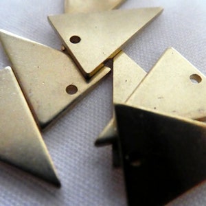 Op de afbeelding: Een groep van zes gouden driehoekige metalen bedels met een gat in elke hoek. De bedels zijn willekeurig gerangschikt op een wit oppervlak.