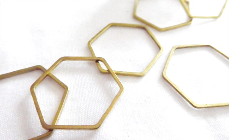 Peut inclure: Une collection de cadres hexagonaux en m&eacute;tal dor&eacute; fin, dispos&eacute;s en un motif l&acirc;che et superpos&eacute;. Chaque cadre est une forme g&eacute;om&eacute;trique simple et ouverte avec une finition m&eacute;tallique lisse, cr&eacute;ant une s&eacute;rie de contours hexagonaux reli&eacute;s.