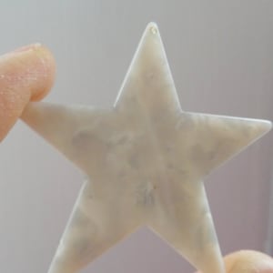 May include: A white star-shaped ornament with a marbled pattern. The ornament has a small hole at the top for hanging.
