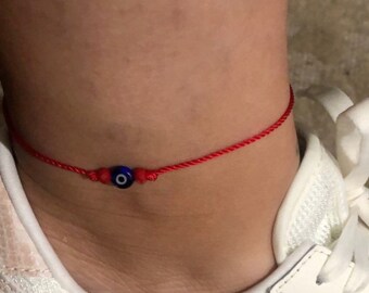 May include: Red string anklet with a blue and white evil eye charm.