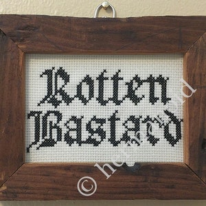 Peut inclure: Point de croix encadré dans un cadre en bois foncé. Le texte noir sur tissu blanc dit "Rotten Bastard" dans une police gothique. Le cadre est de couleur marron foncé et possède un crochet de suspension en métal.