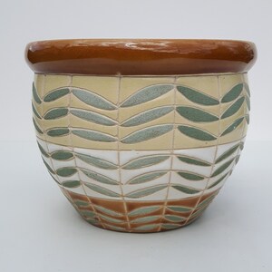 May include: A brown ceramic planter with a geometric pattern of green leaves on a white and brown background.