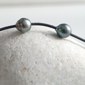 May include: A black leather cord necklace with three dark gray pearls.