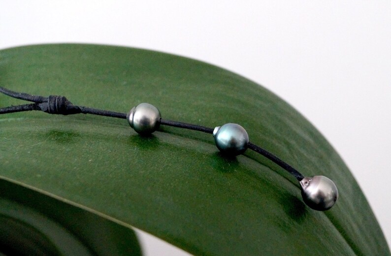 May include: A black leather cord necklace with three dark green pearls.