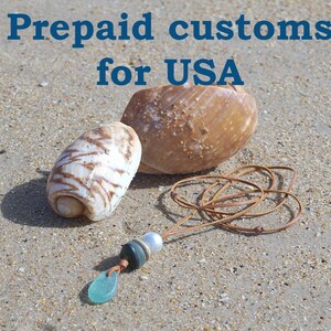 May include: A necklace featuring a brown leather cord with a light blue sea glass pendant, a dark grey bead, and a white pearl bead, accompanied by two seashells. The text "Prepaid customs for USA" is displayed in blue at the top of the image.