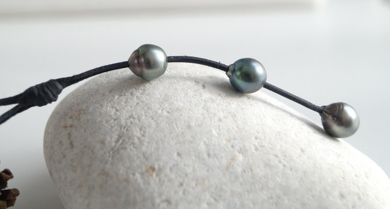 May include: A black leather cord necklace with three dark gray pearls.