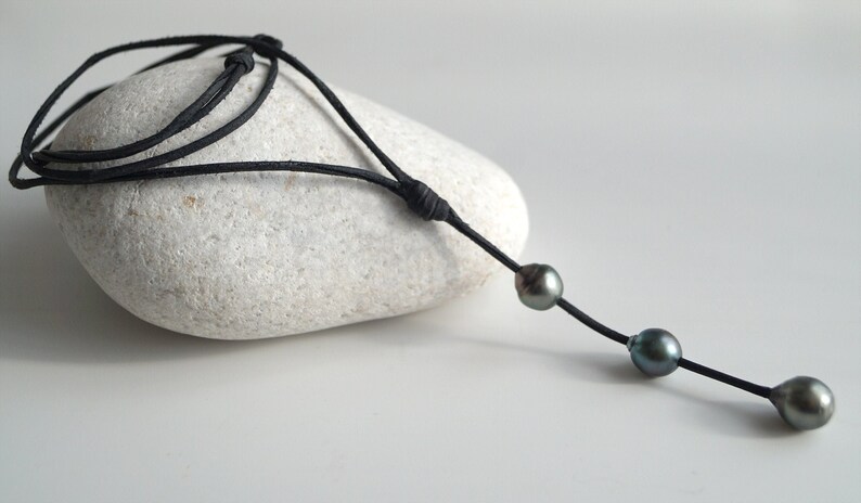 May include: A black leather cord necklace with three dark green pearls.