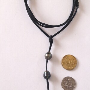May include: A black leather cord necklace with three dark grey pearls. The necklace is shown with two coins for size reference.