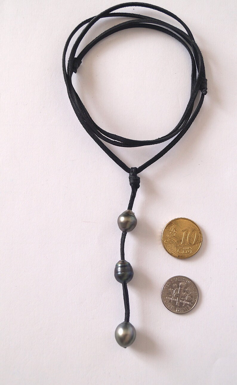 May include: A black leather cord necklace with three dark grey pearls. The necklace is shown with two coins for size reference.