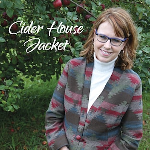 May include: A woman wearing a brown, red, and blue patterned jacket with a white turtleneck shirt, holding a basket of red apples. The basket is woven with brown, yellow, and blue stripes. The text "Cider House Jacket" is written in white cursive letters at the top of the image. The text "Snapdragon Studios" is written in green and white letters at the bottom of the image. The text "No. 153" is written in black letters at the bottom left of the image.