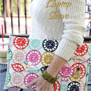 May include: A colourful laptop sleeve with a retro design featuring a repeating pattern of colourful circles. The sleeve is made of fabric and has a flap closure. The text "Heigh-ho Laptop Sleeve" is written in gold lettering on the sleeve. The text "Sapdragon Studios" is written in green lettering on the bottom left corner of the sleeve. The text "No. 154" is written in black lettering on the bottom right corner of the sleeve.