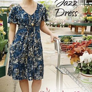 May include: A woman wearing a blue and white floral print dress with short sleeves and a V-neck. She is standing in a greenhouse and holding a shopping trolley. The text "Summer Jazz Dress" is written in black on a white background. The text "No. 141" is written in black on a white background. The text "Sapdragon Studios Clothing Patterns" is written in black on a white background.