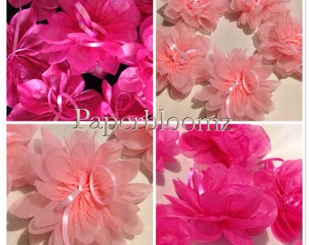 May include: A collection of pink and light pink tissue paper flowers. The flowers are arranged in a circle and are tied together with pink ribbon. The flowers are made of multiple layers of tissue paper and have a delicate, ruffled appearance.