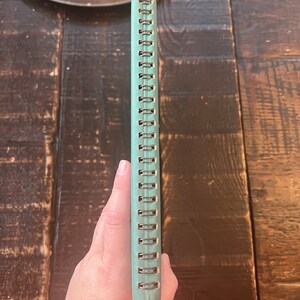 以下が含まれることがあります： 金属製のスパイラルバインディングが付いたターコイズブルーのノート。ノートは閉じられており、背表紙が見えています。