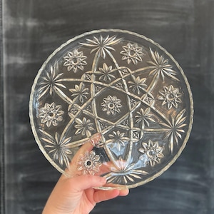 May include: A clear glass serving plate with a starburst pattern. The plate has a scalloped edge and is perfect for serving desserts or appetizers.