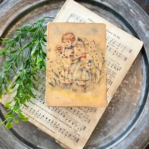 May include: Vintage postcard featuring a watercolour illustration of two children in a field of daisies. The children are wearing dresses and are holding flowers. The text on the postcard reads "Years Go By".