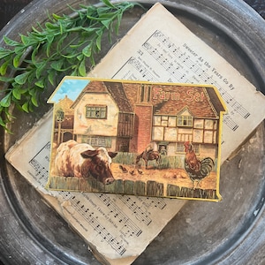 May include: A rectangular tin box with a house-shaped top edge, featuring a vintage illustration of a farm scene with a cow, a rooster, and a person on horseback. The text "Farm Set" is printed in a decorative font on the upper right side.