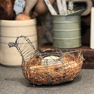 May include: A wire chicken-shaped egg basket with a nest of straw and three white eggs inside.