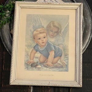 May include: A framed vintage print depicting a young boy and a guardian angel. The boy is wearing a blue sailor suit and is looking at a turtle in the water. The angel is wearing a white dress and has her wings spread out. The print is titled "His Guardian Angel 1933".