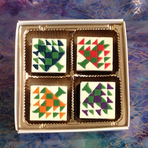 May include: A box of four chocolate squares, each with a different geometric pattern in green, red, orange, and purple.