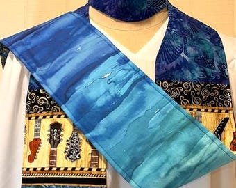 Könnte beinhalten: Eine blaue und türkisfarbene Priesterstola und eine passende Kappe. Die Stola zeigt ein Aquarelldesign, Musikinstrumente und Klaviertasten. Die Kappe hat ein Wirbelmuster. Die Stola wird über einem weißen Kleidungsstück getragen.