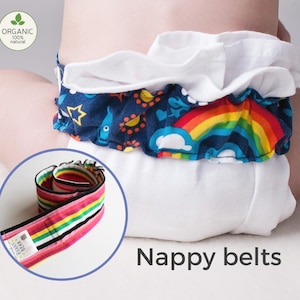 May include: A colorful, striped nappy belt with the words "Nappy Belts" printed on the label. The belt is rolled up and displayed on a white surface. The belt is made of organic cotton and is 100% natural.