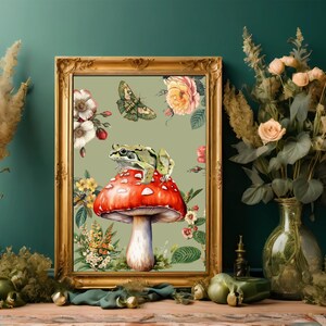 May include: A framed botanical print featuring a red mushroom with a white-spotted cap, a green frog, and a butterfly. The print is surrounded by floral and botanical elements, set in a gold ornate frame. The background is a muted green.