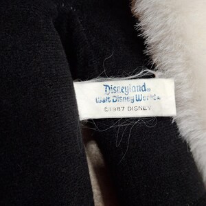 May include: Close-up of a plush toy with black and red fabric, and white fur trim. A tag reads "Disneyland, Walt Disney World, &copy;1987 DISNEY". The toy appears to be a vintage collectible.