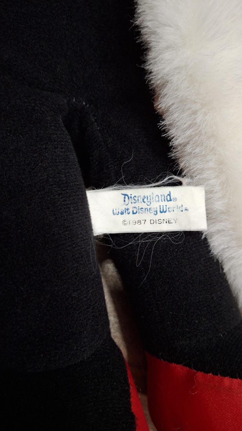 May include: Close-up of a plush toy with black and red fabric, and white fur trim. A tag reads "Disneyland, Walt Disney World, &copy;1987 DISNEY". The toy appears to be a vintage collectible.